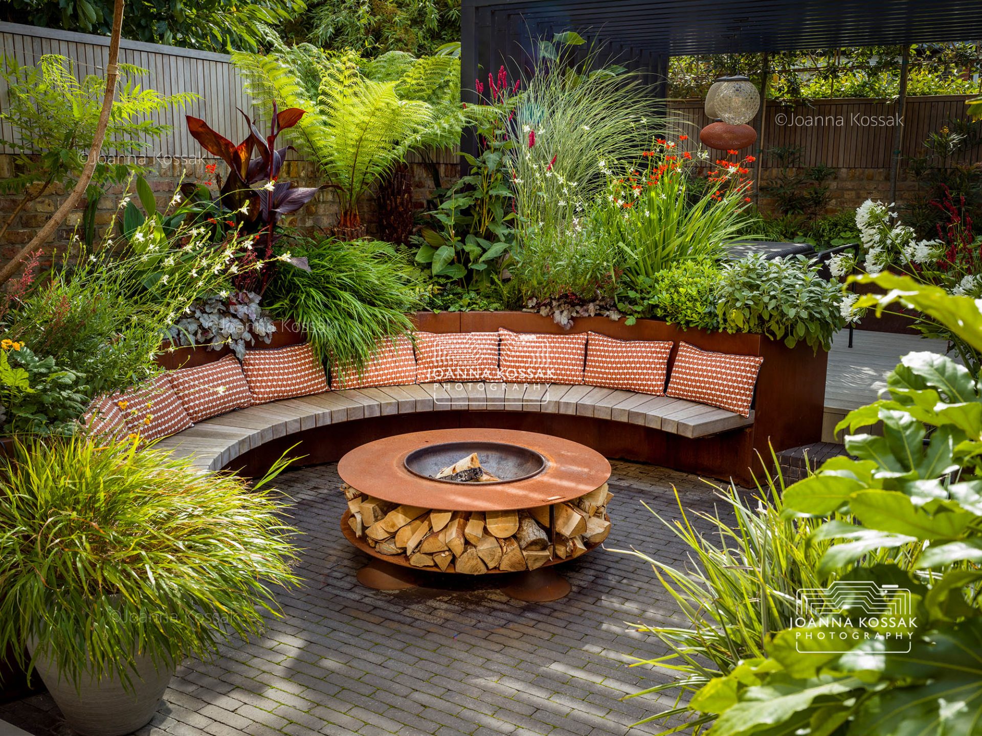 Wide view of an urban garden with a curved bench and fire pit on a summer day in August