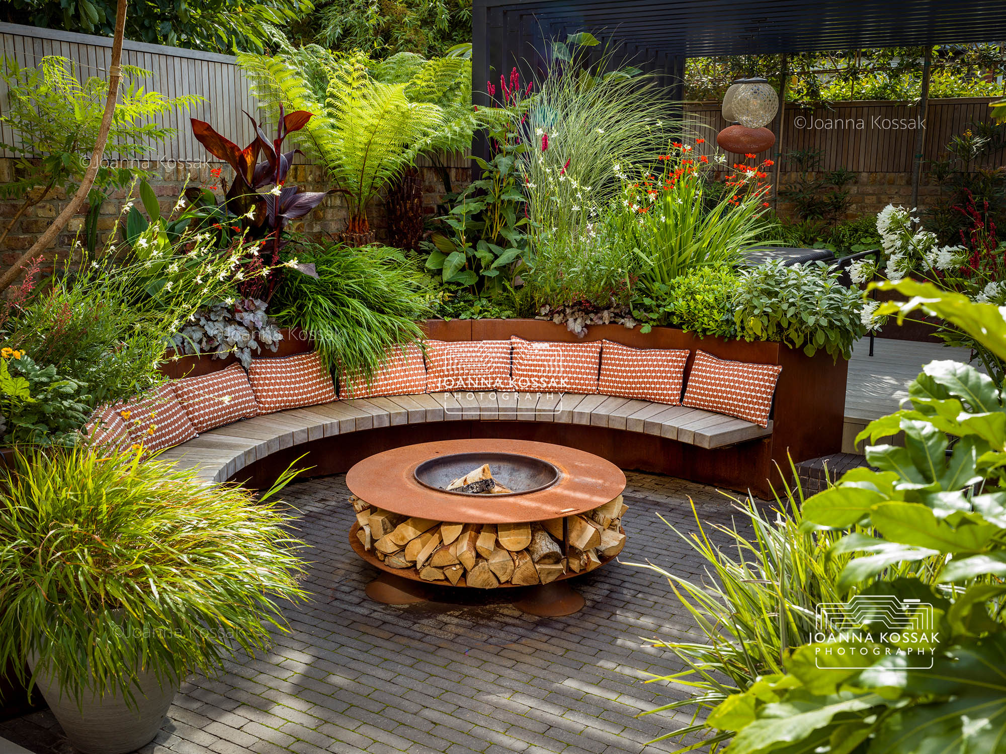 Wide view of an urban garden with a curved bench and fire pit on a summer day in August